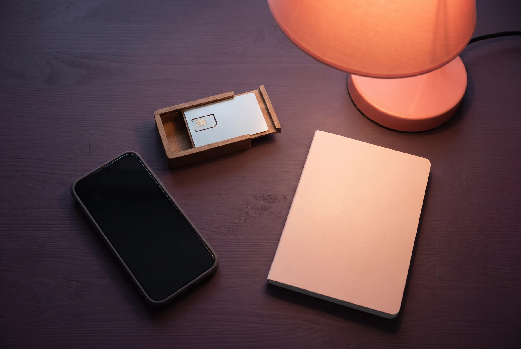 Phone, lamp, device card and notebook on plum desk
